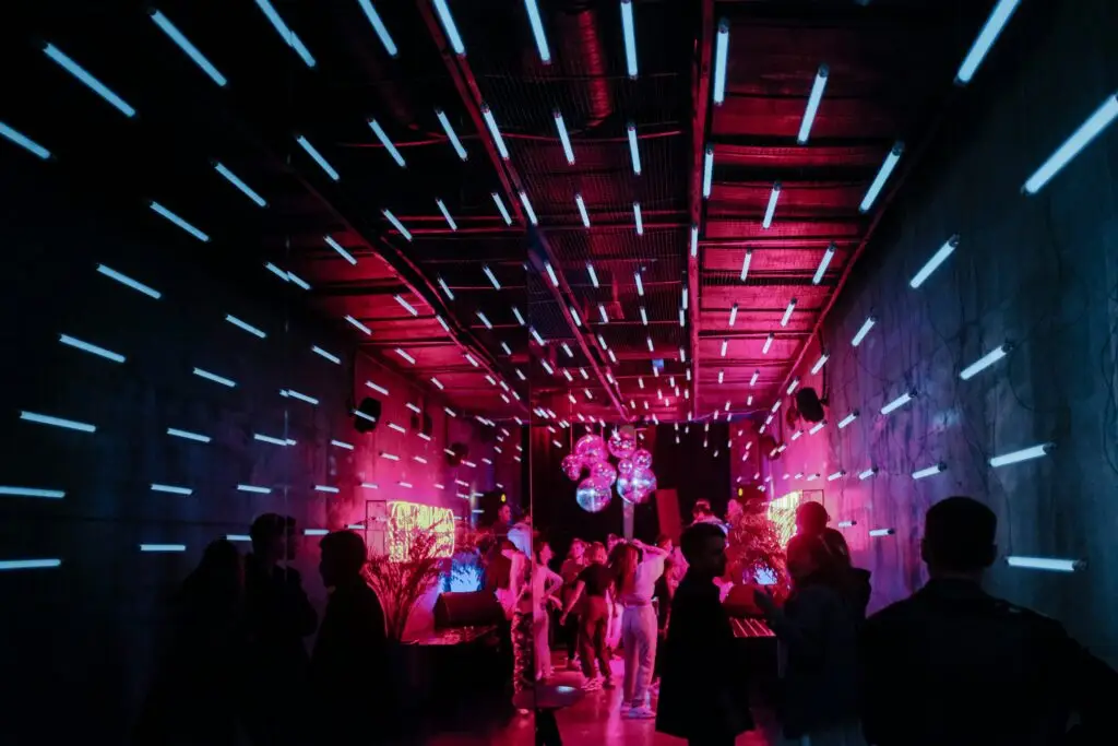Our Services neon lit pink and purple bar/event space that is full of decor and patrons in the background